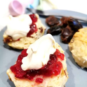 Date scones served on a plate and topped with raspberry jam and cream
