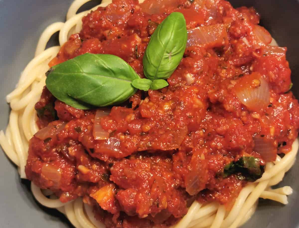 The pasta sauce is served in a bowl on top of gluten free spaghetti with fresh basil leaves