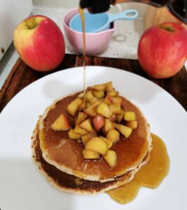 maple syrup being poured onto the apple cinnamon pancakes