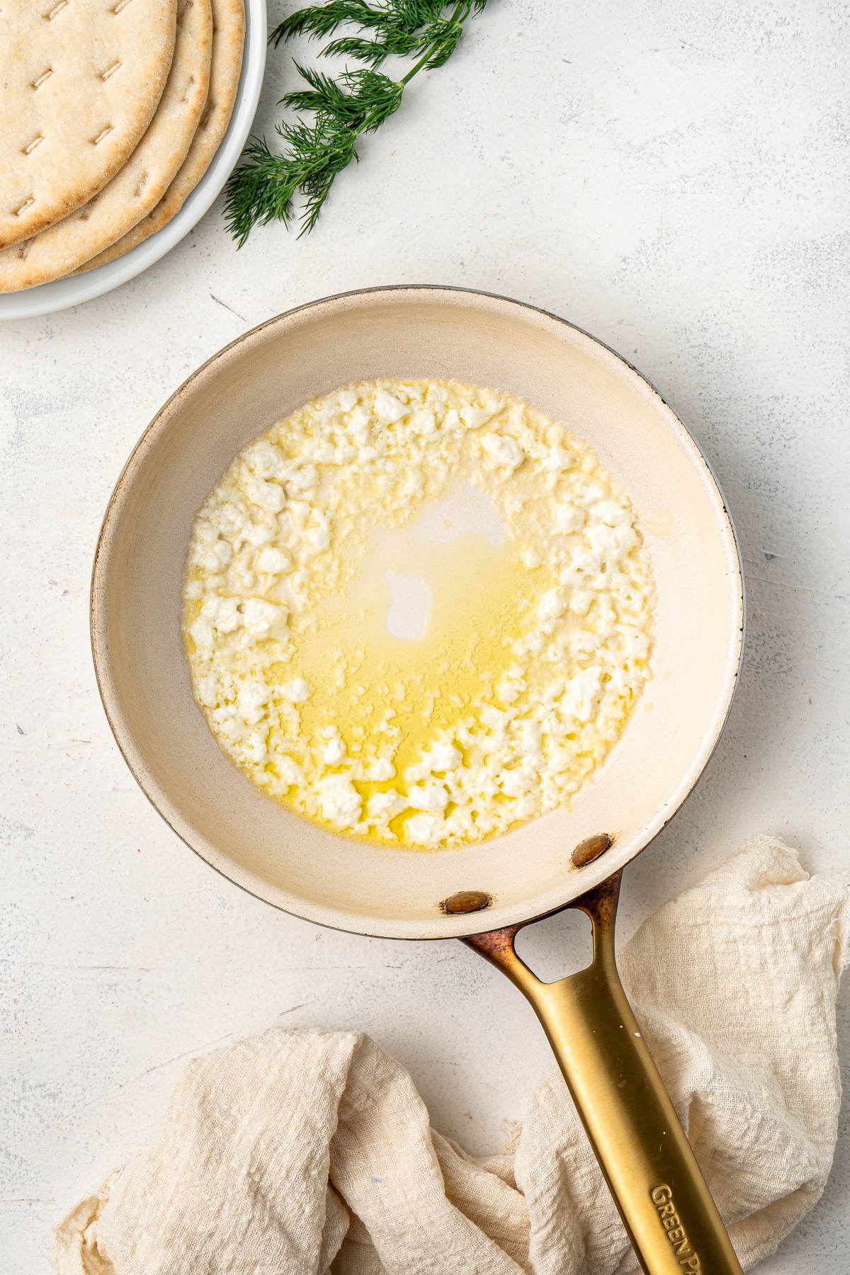 A pan on the counter, with oil and crumbled feta in a ring, leaving the center of the pan clear.