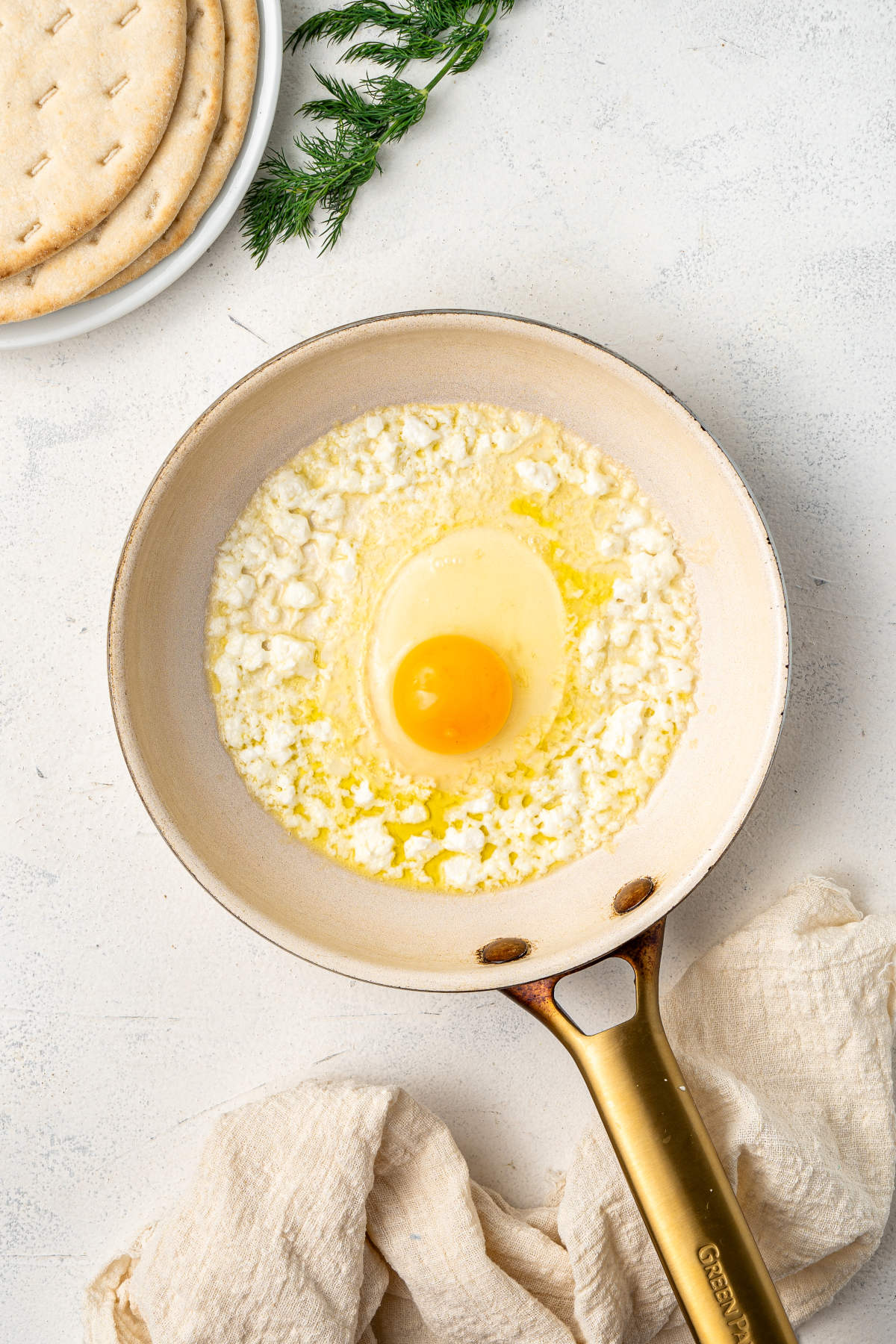The pan now has the egg cracked in the center, ready to be fried alongside the feta.