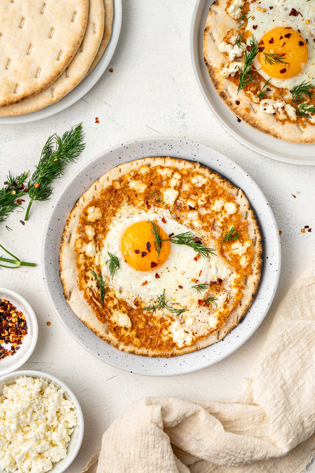 The eggs and feta served on top of pita bread on a white plate, garnished with chili and dill.