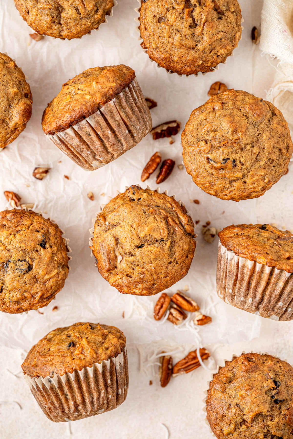 The finished muffins, still in their muffin cases, spread out on the kitchen counter with some pecan nuts.