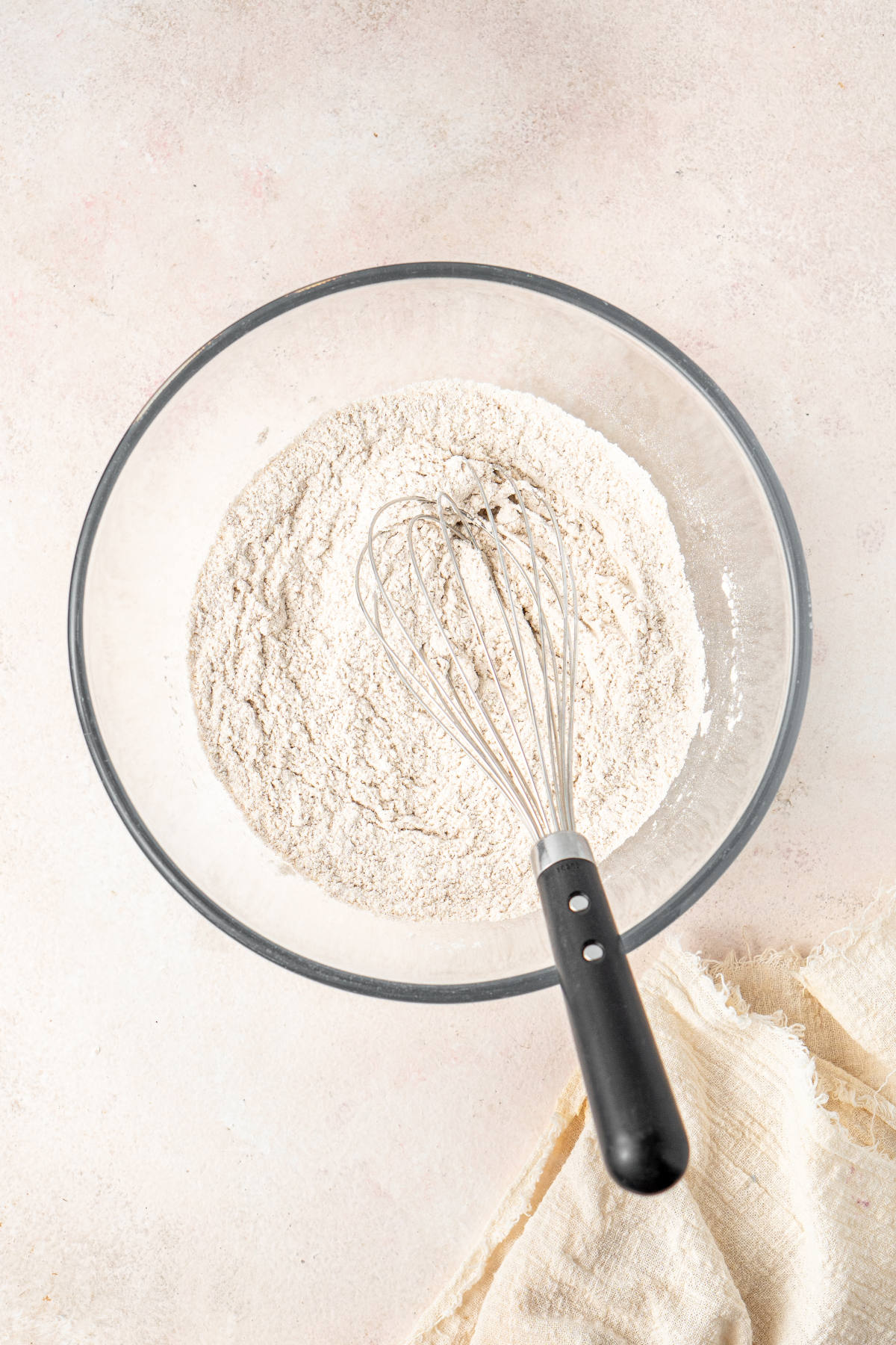 A glass mixing bowl with dry ingredients and a whisk resting in it.