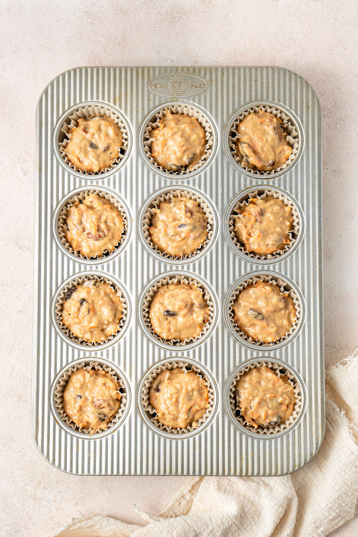A 12-muffin muffin tray filled with muffin cases and batter, ready to go in the oven.