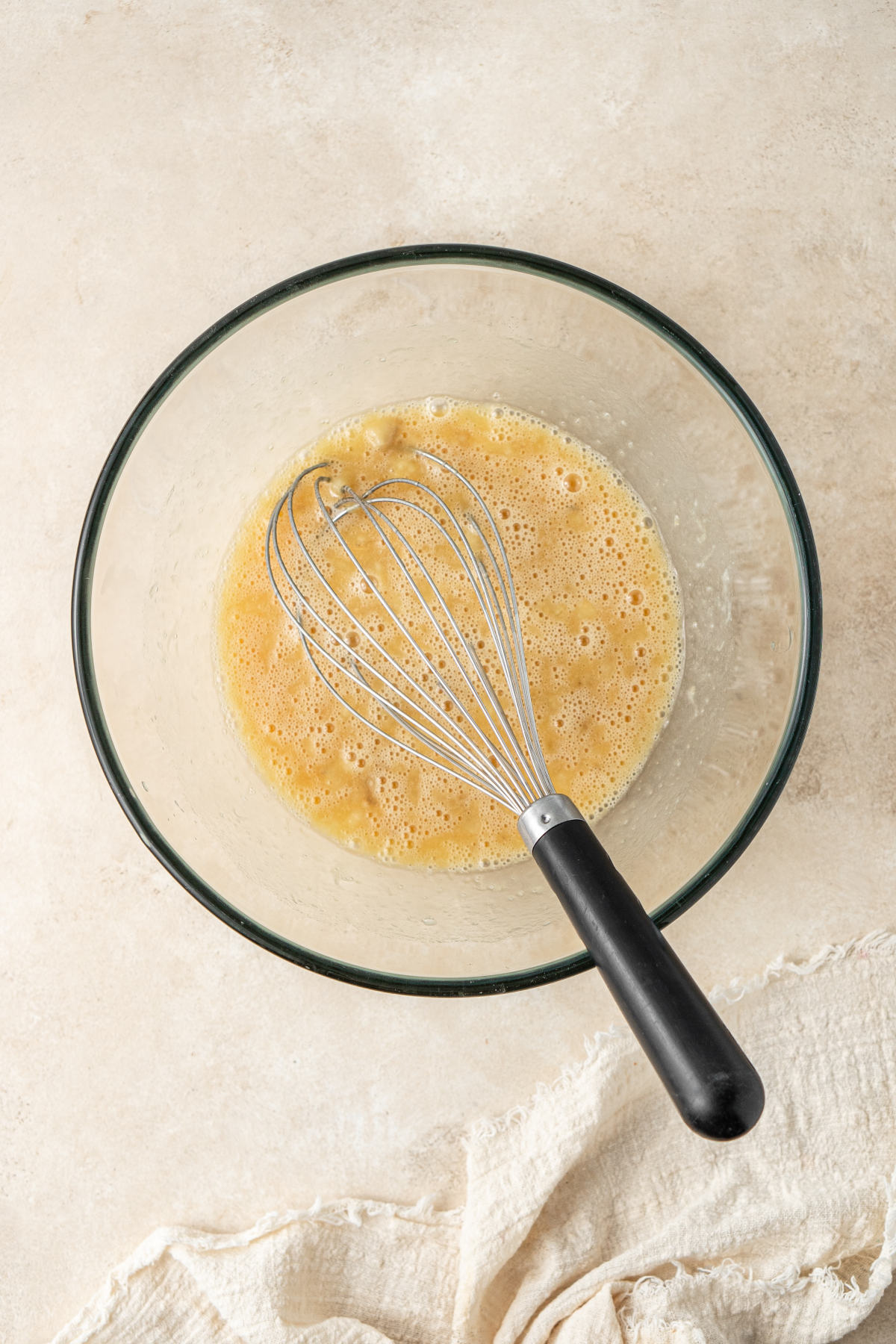 A glass mixing bowl with the wet ingredients of the muffins and a whisk.