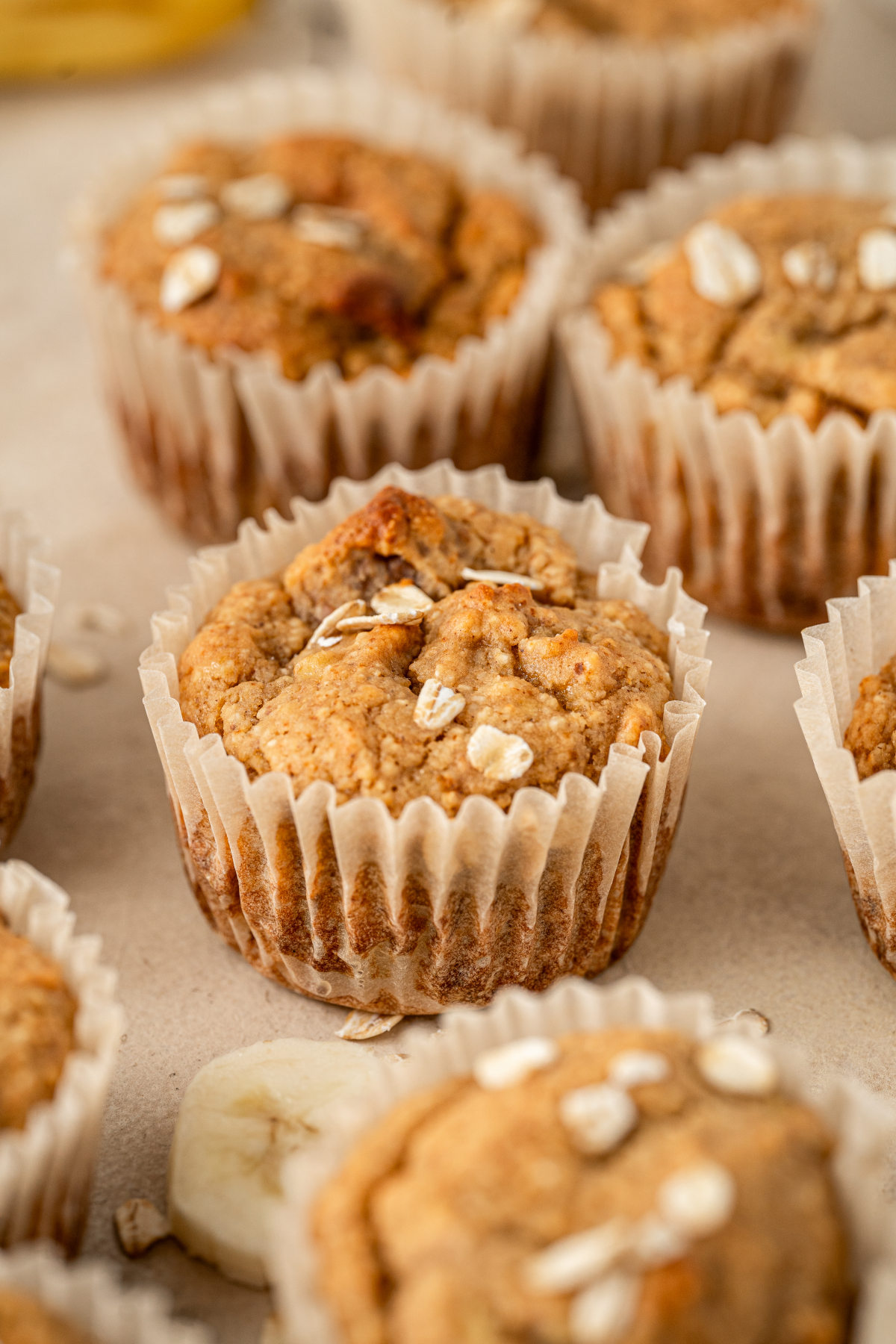 Banana protein muffins laid out on a kitchen counter amongst some sprinkled oats and slices of banana.