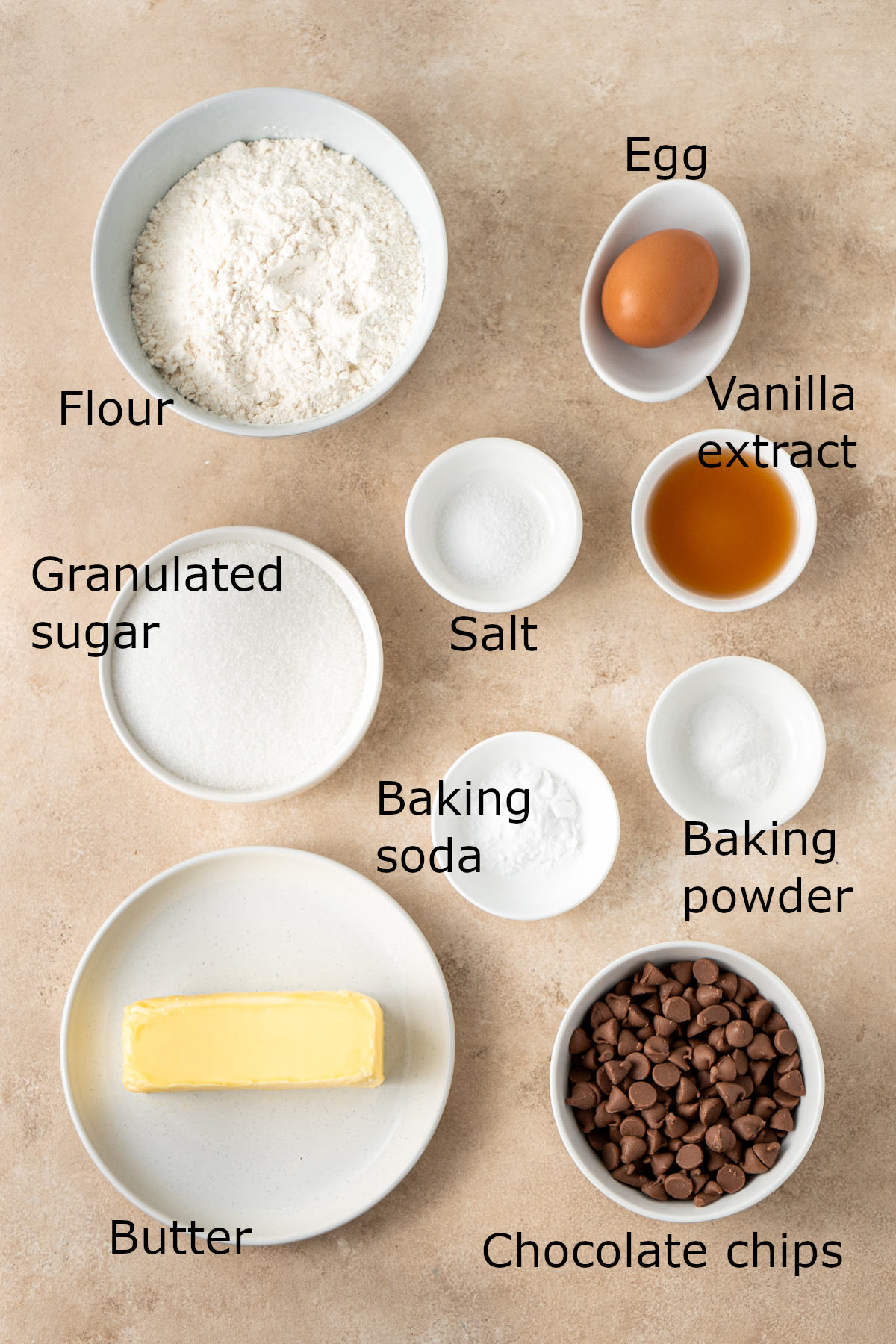 The ingredients for the cookies laid out in white bowls on a brown kitchen counter.