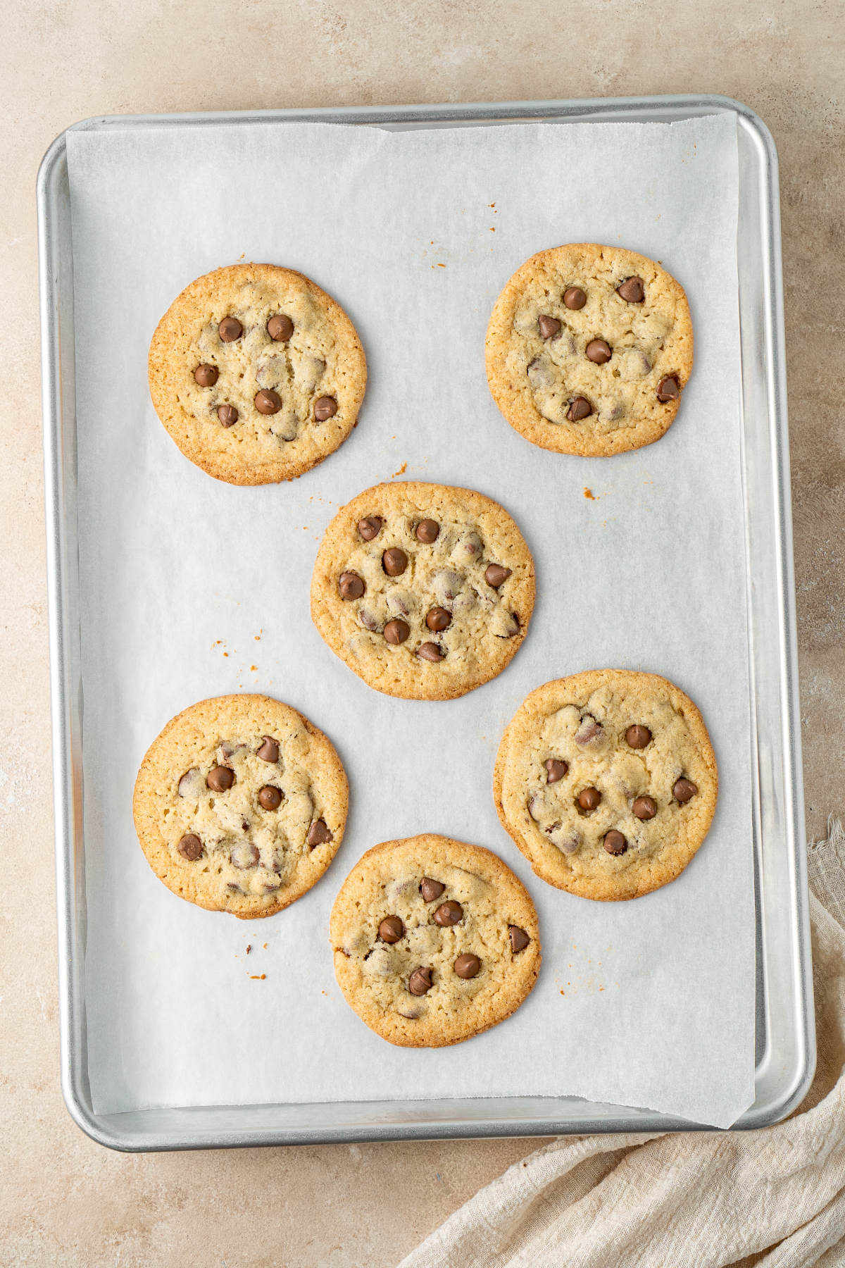 Six baked cookies on a baking-paper lined baking tray, ready to cool.