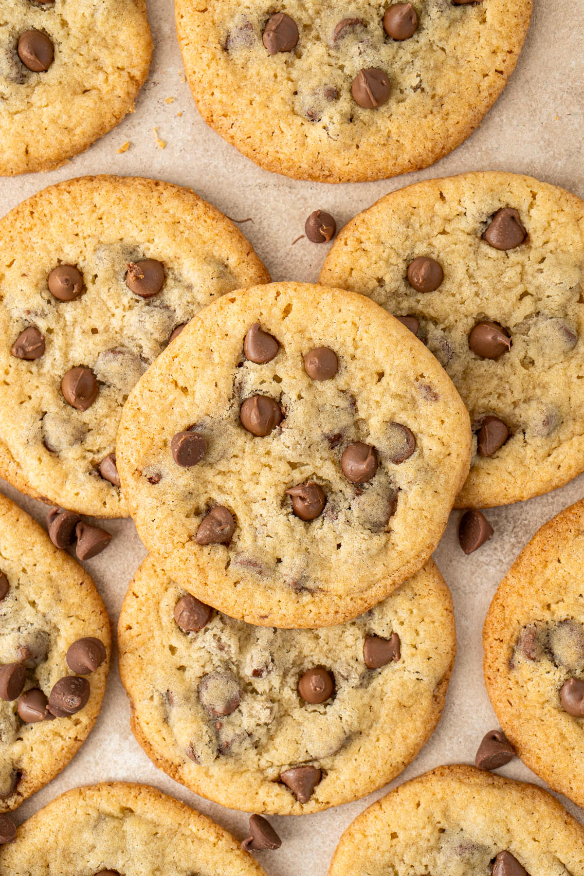 A close-up image of a pile of cookies surrounded by chocolate chips all sitting on a kitchen counter.
