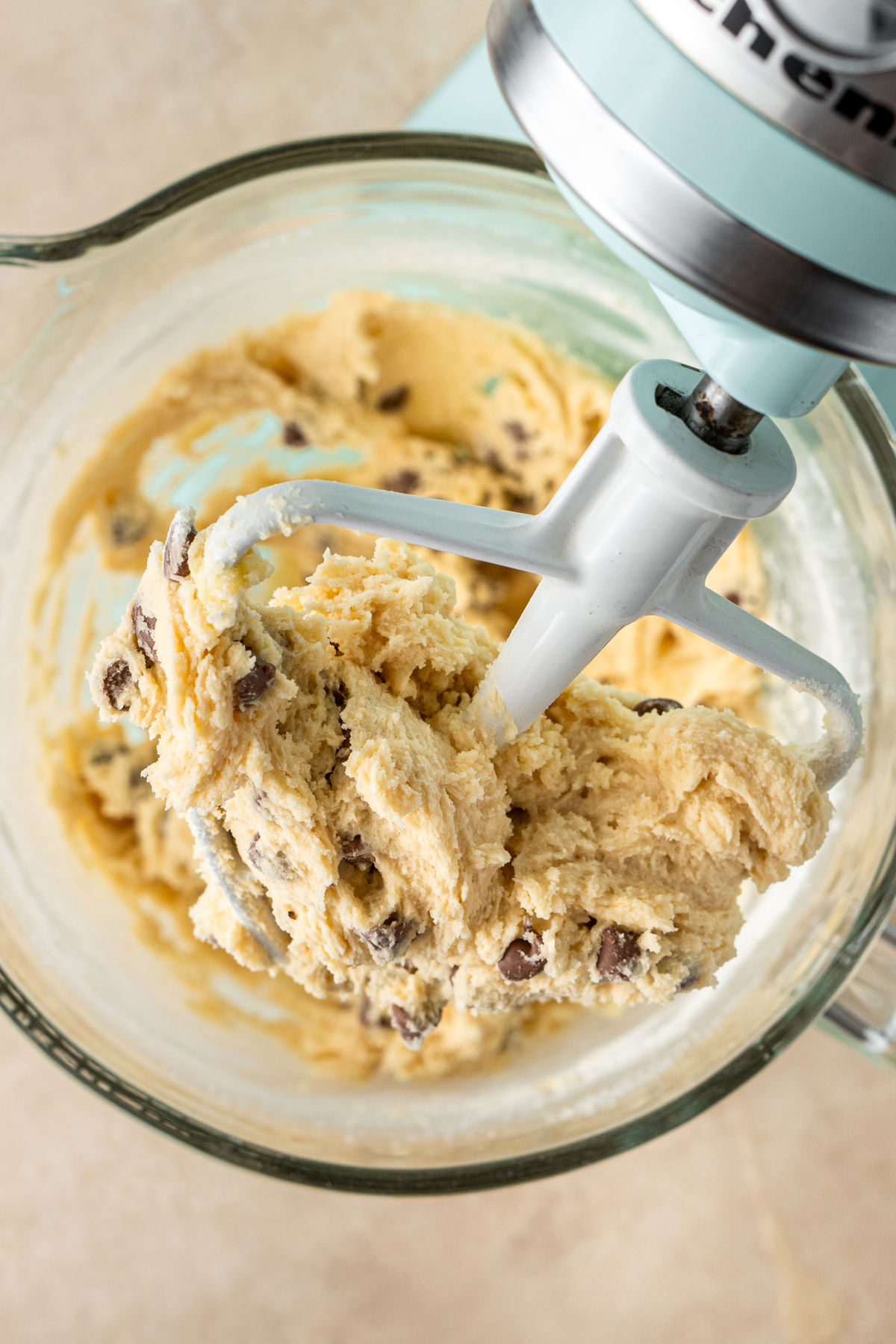 A close up of the whisk of a stand mixer, coated with chocolate chip cookie dough.