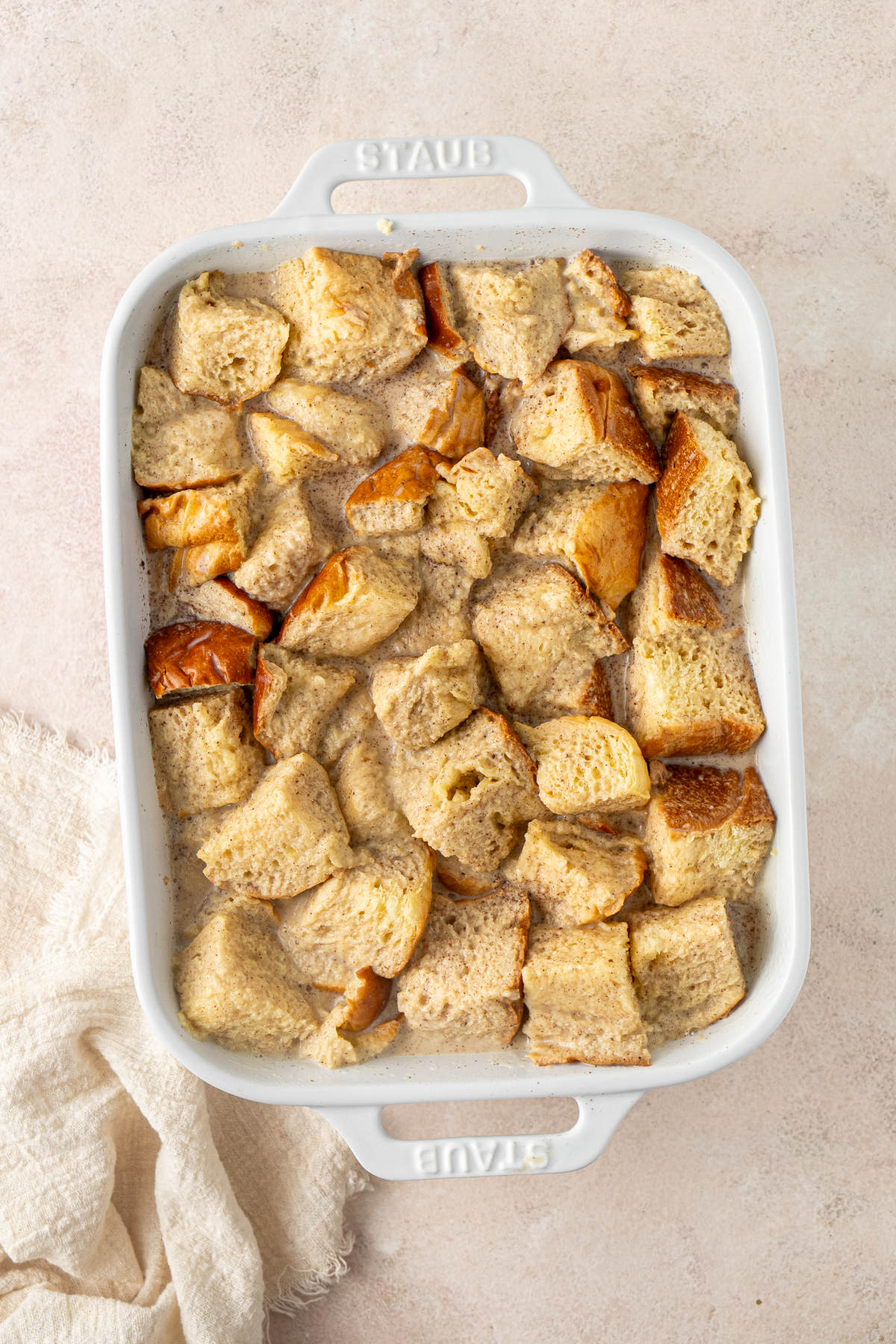 A white baking dish filled with cubes of brioche soaked in custard.