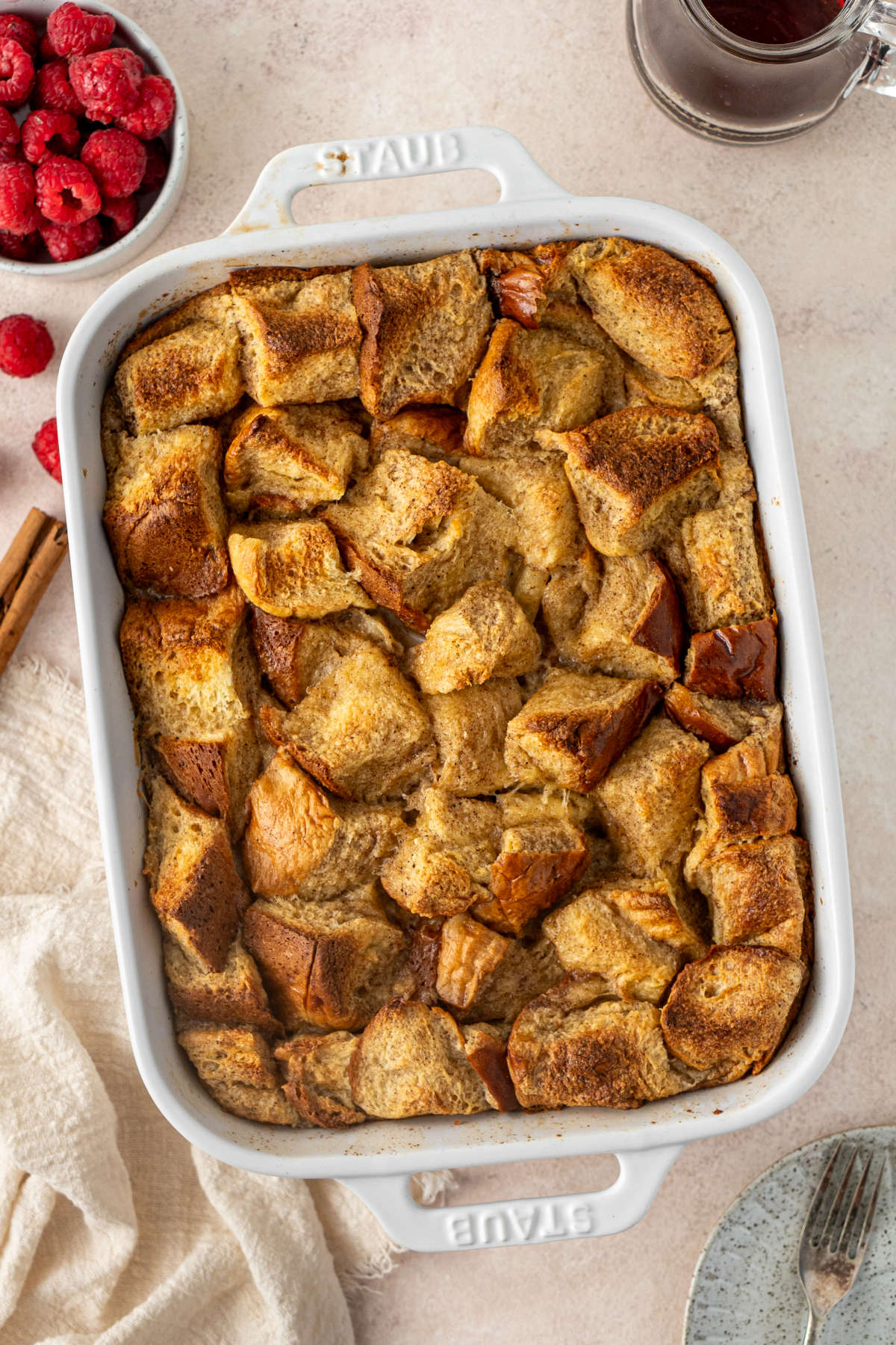 A baking dish filled with freshly baked French toast which is being left to cool next to a bowl of raspberries on a kitchen counter.