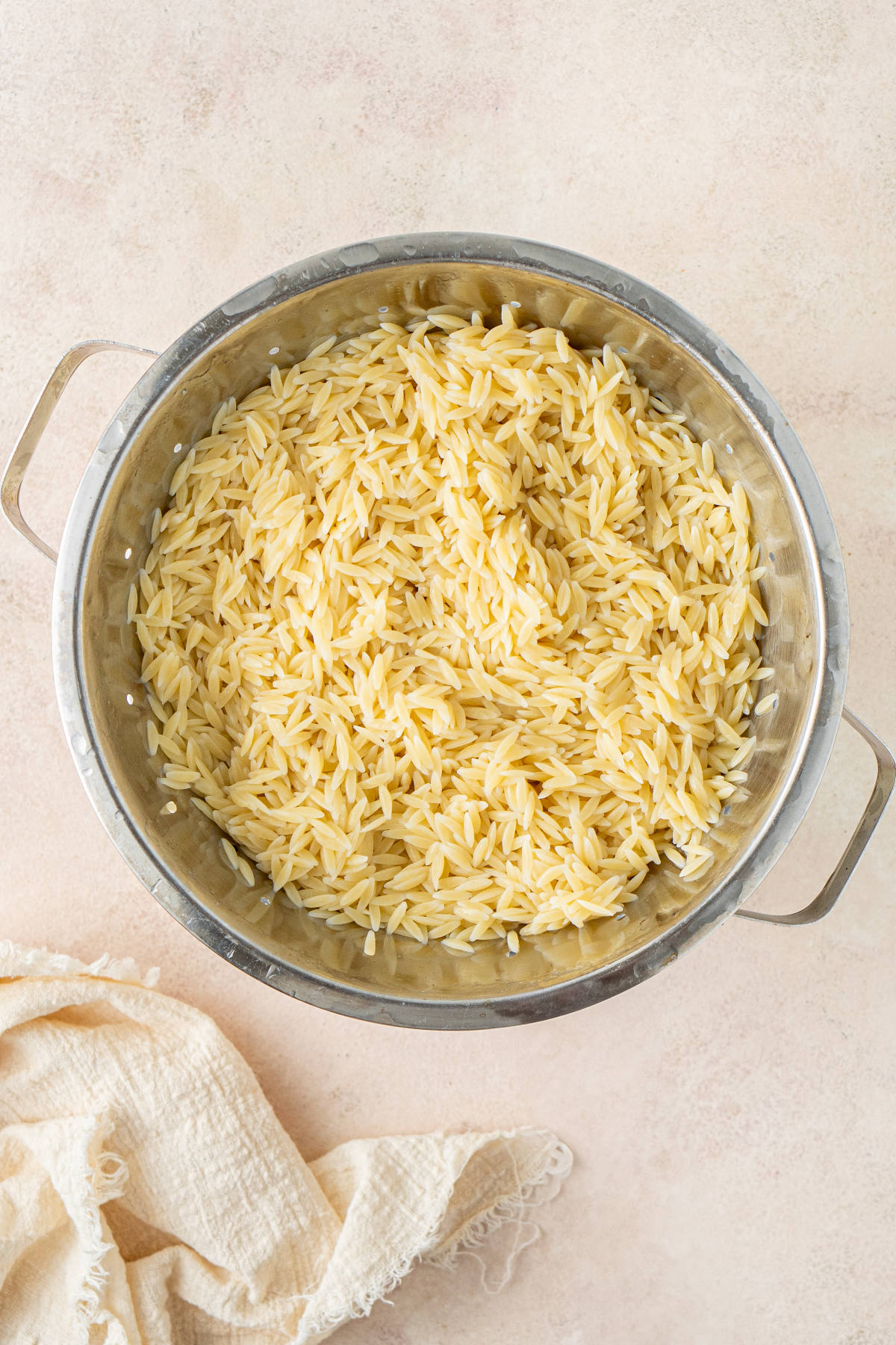 A large metal colander filled with cooked orzo pasta.