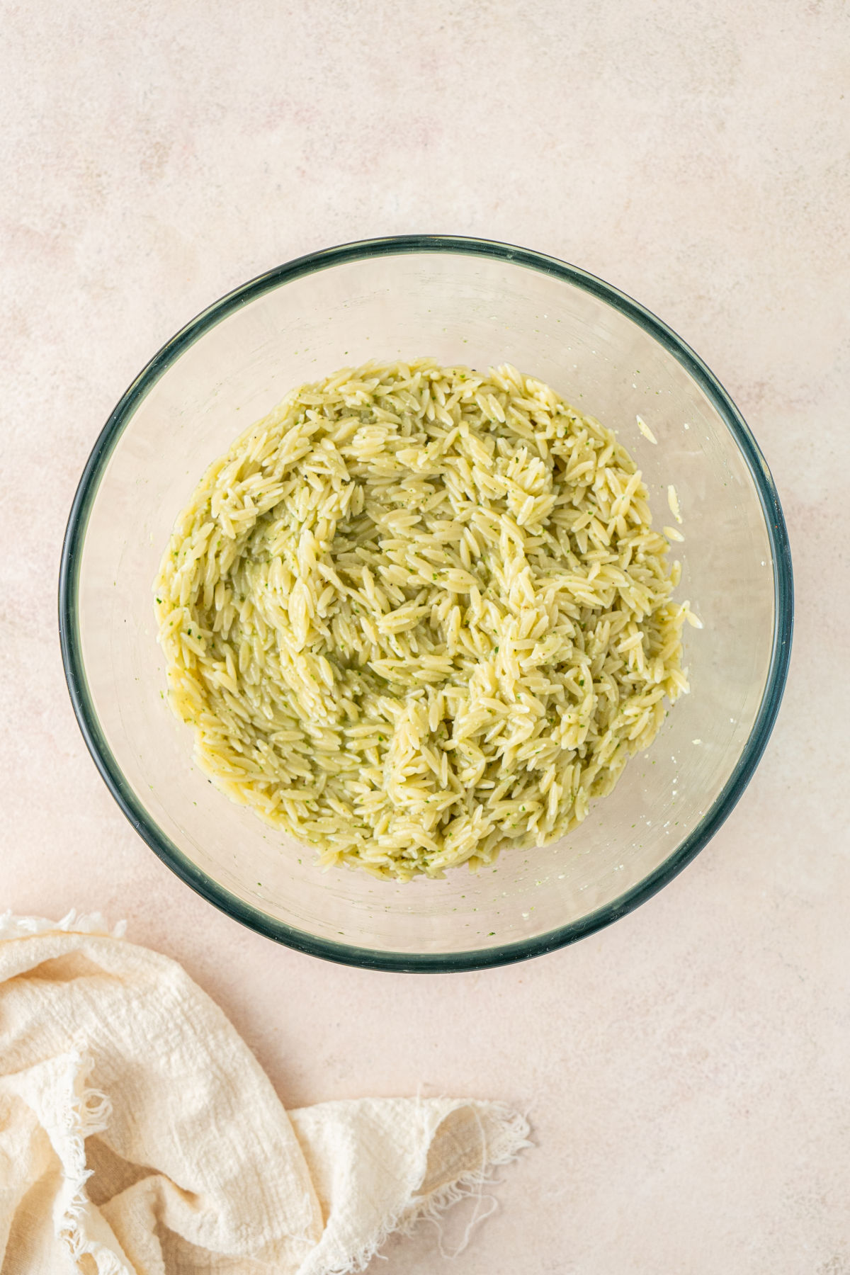 A large glass mixing bowl half-filled with orzo that has been tossed in dressing.