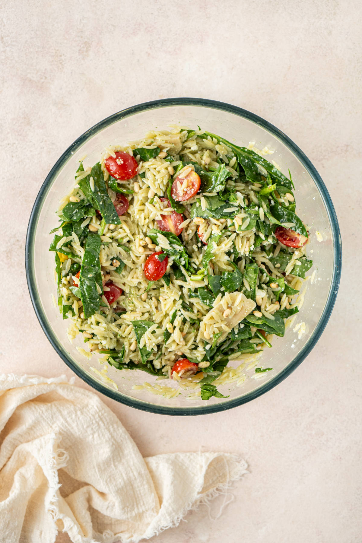 A glass mixing bowl filled with a mix of salad ingredients, well combined.