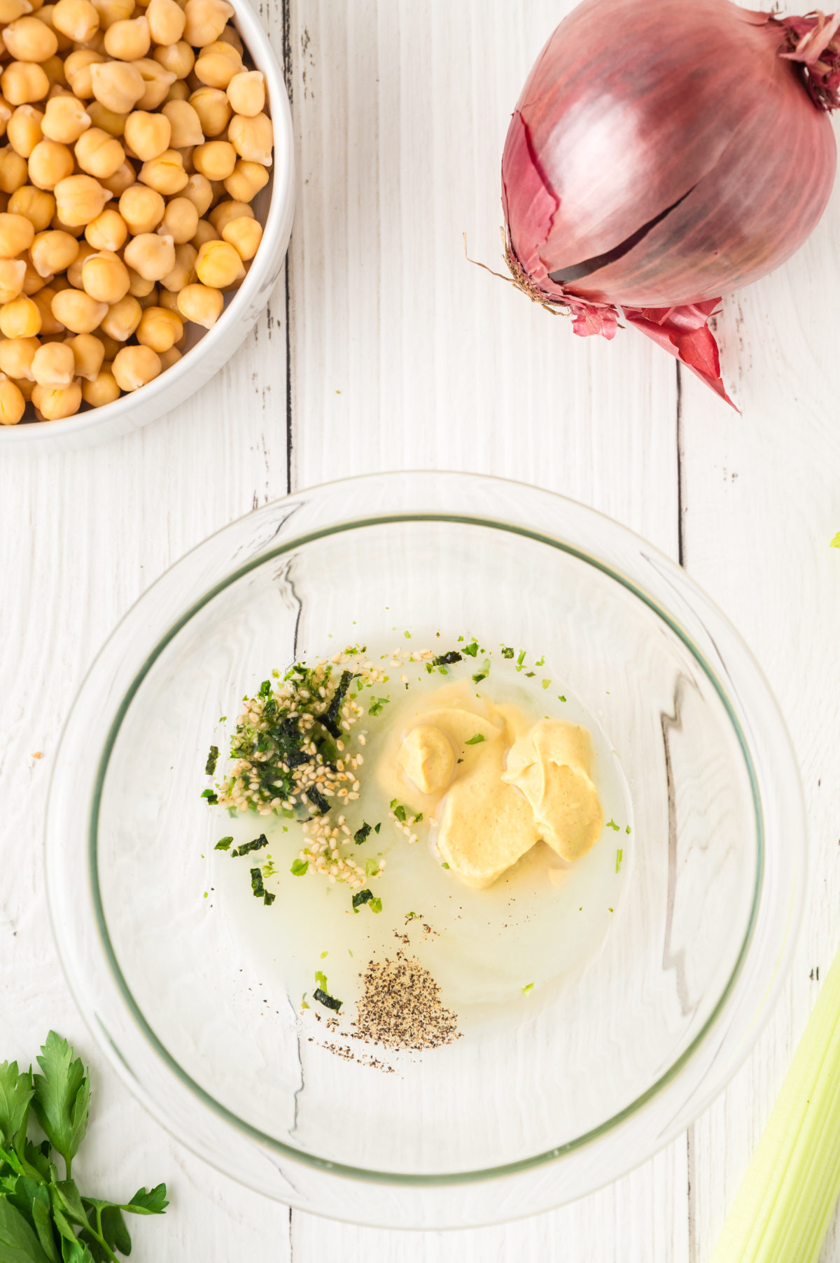A glass mixing bowl viewed from above, containing the unmixed ingredients for our salad dressing.