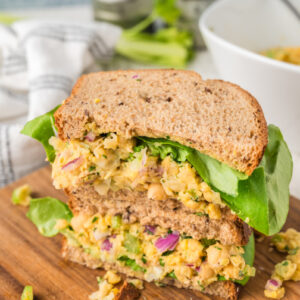 Two halves of a chickpea tuna salad sandwich with lettuce, sitting on a wooden chopping board.