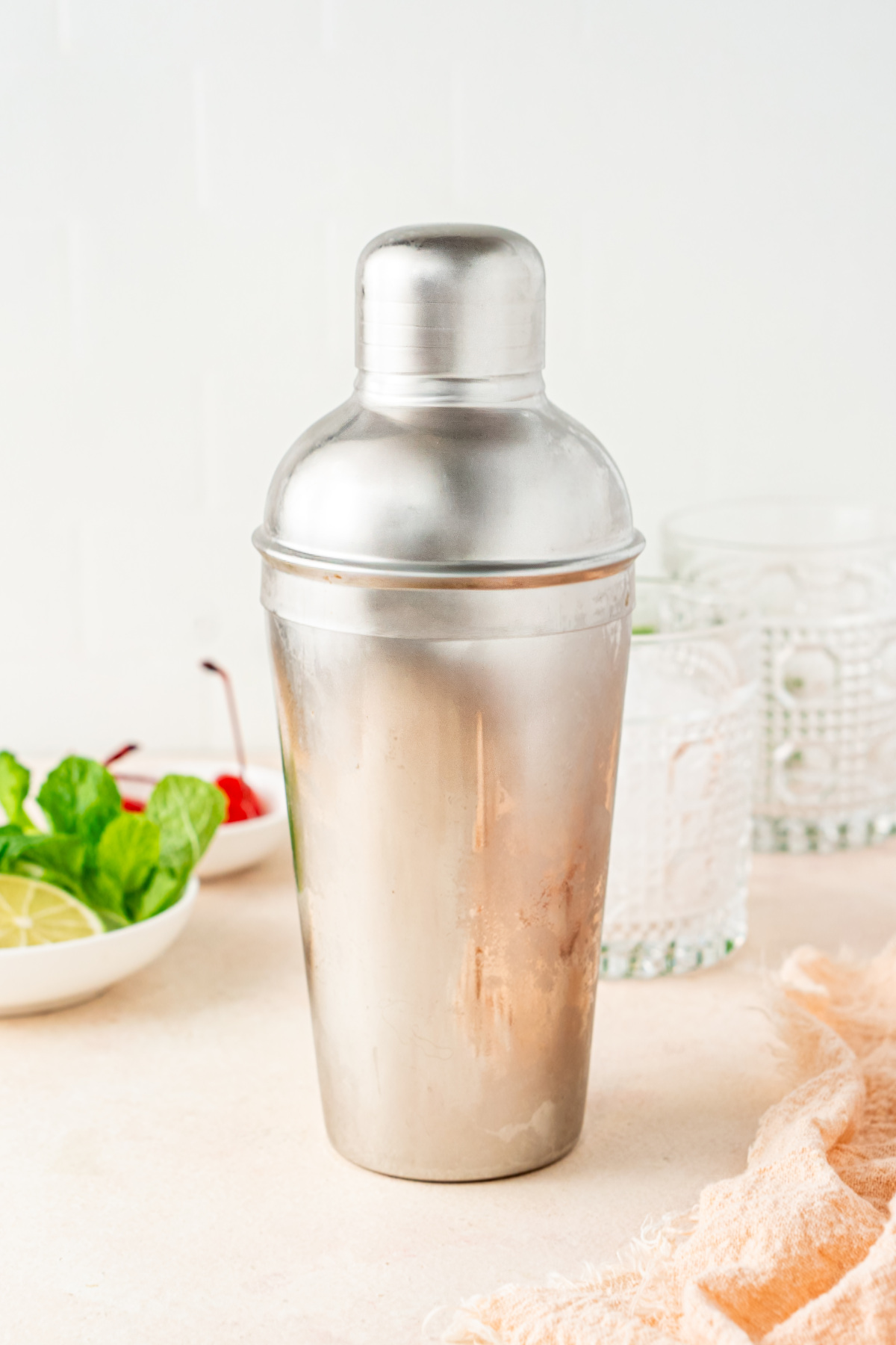 A chilled metal cocktail shaker sitting closed next to glasses and garnishes.