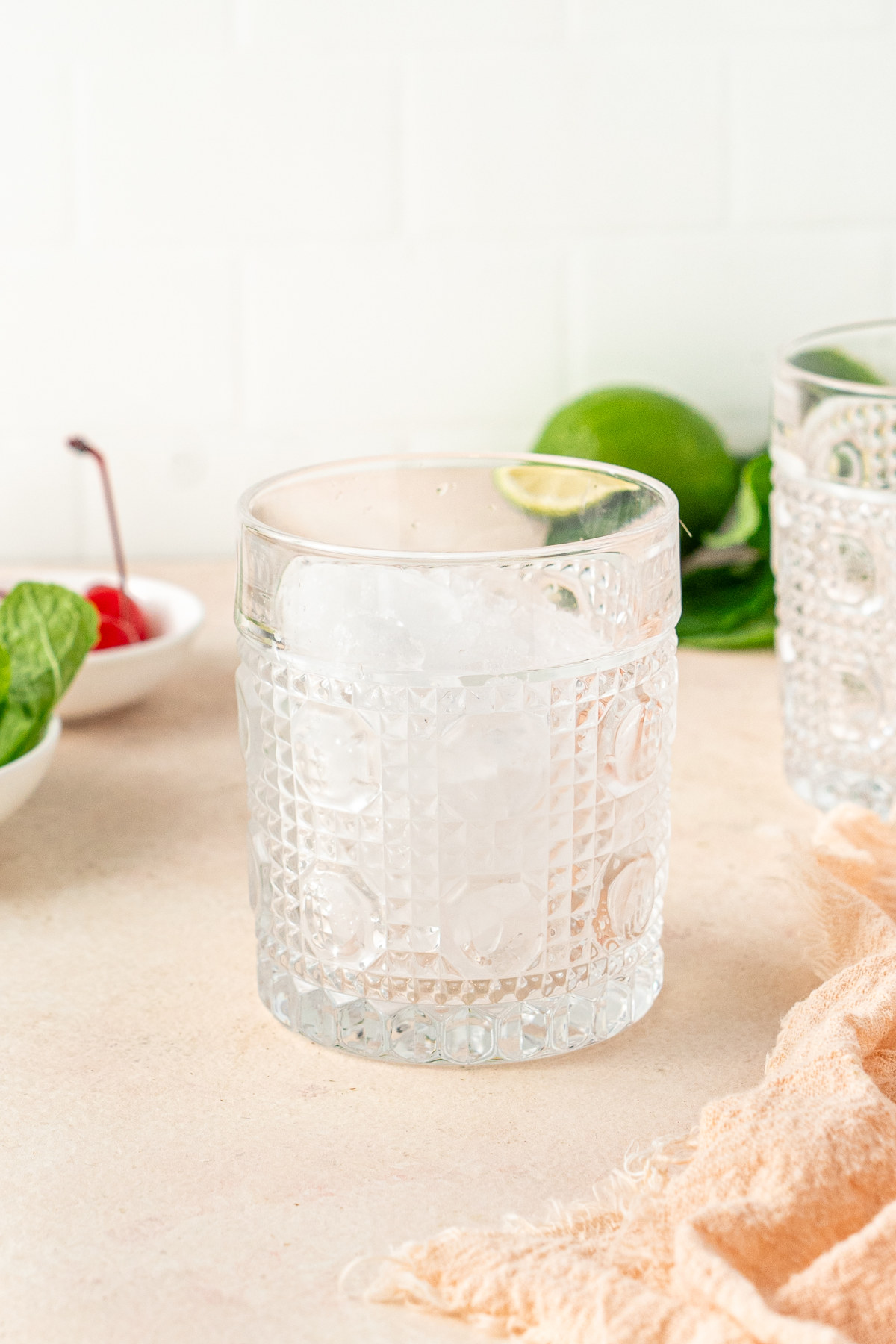 A glass filled with crushed ice next to another glass and some garnishes.