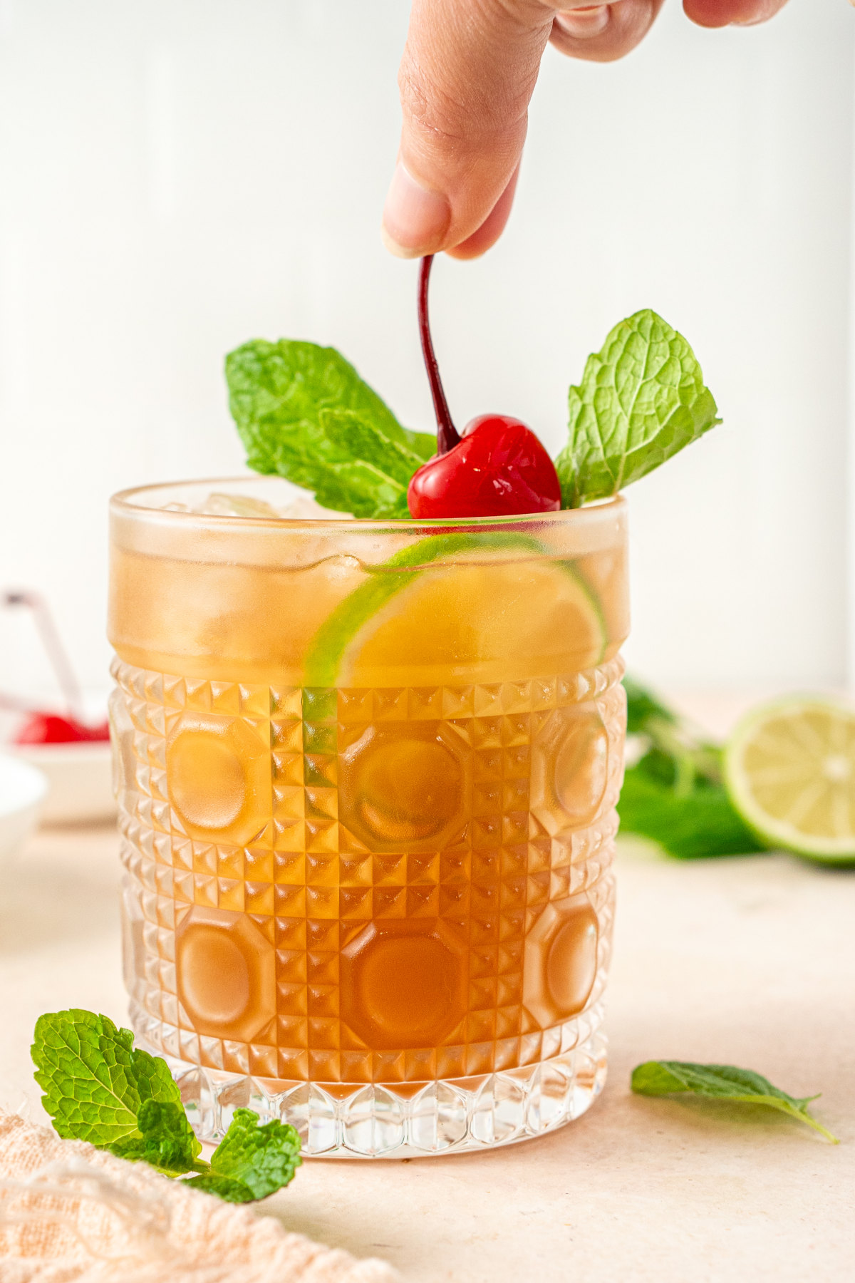 A cocktail being garnished with mint, lime and a maraschino cherry.