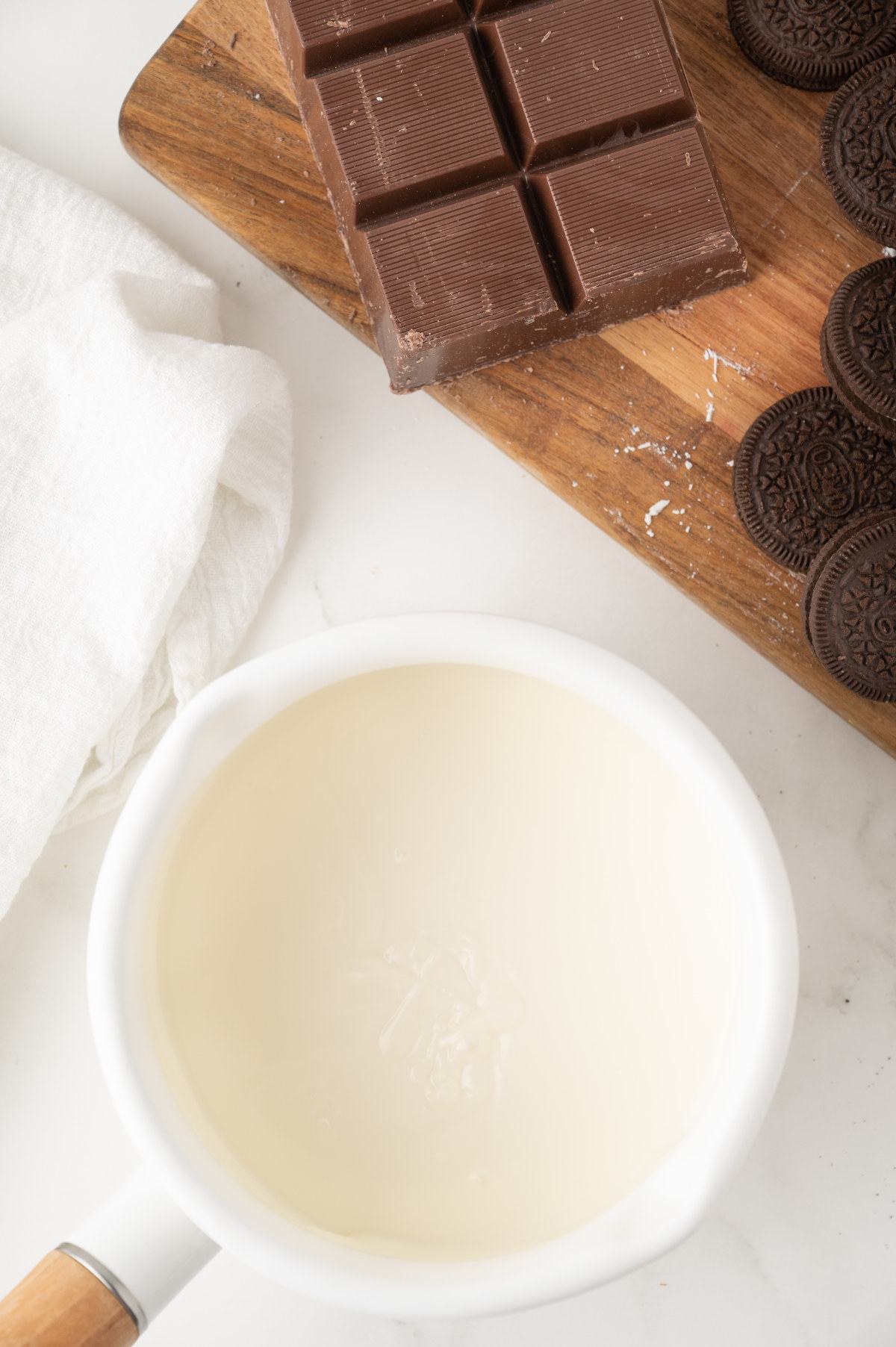 A small white saucepan with melted vanilla almond bark filling it, beside the rest of the ingredients.