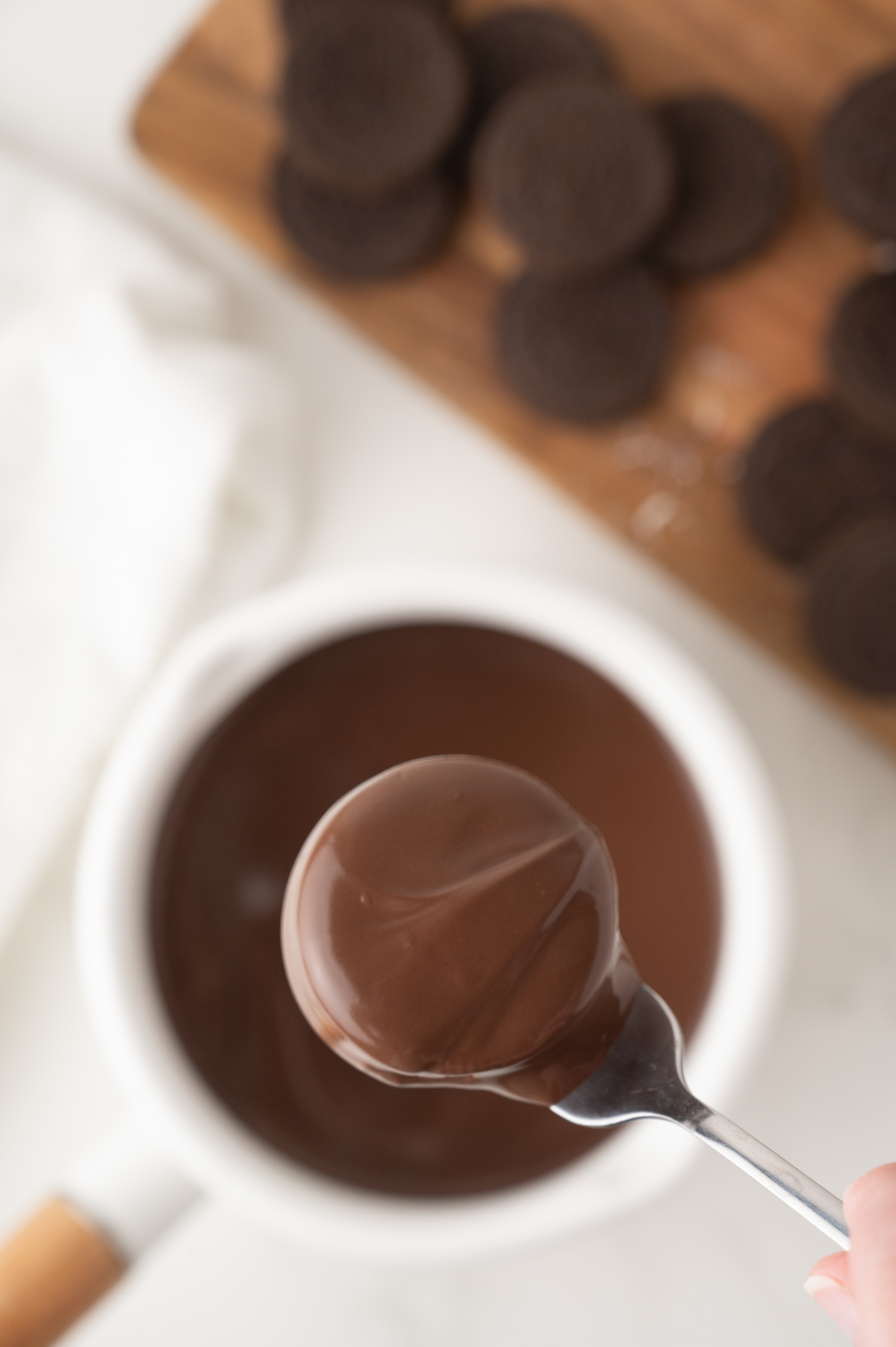 A fork holding a chocolate covered Oreo that has just been dipped into a saucepan of melted chocolate almond bark.
