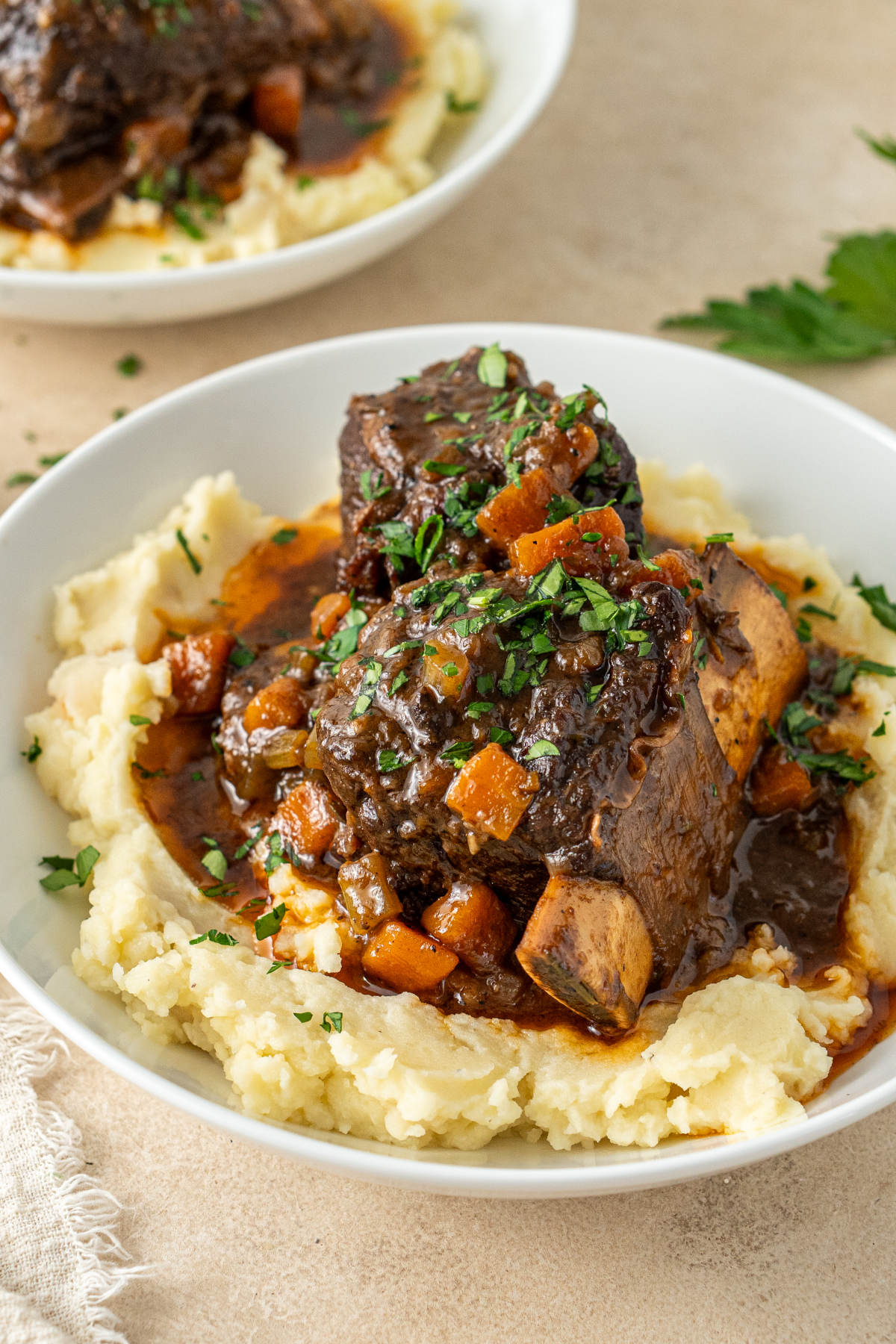 A plate of mashed potatoes over which a hearty serving of beef has been spooned, and garnished with parsley.