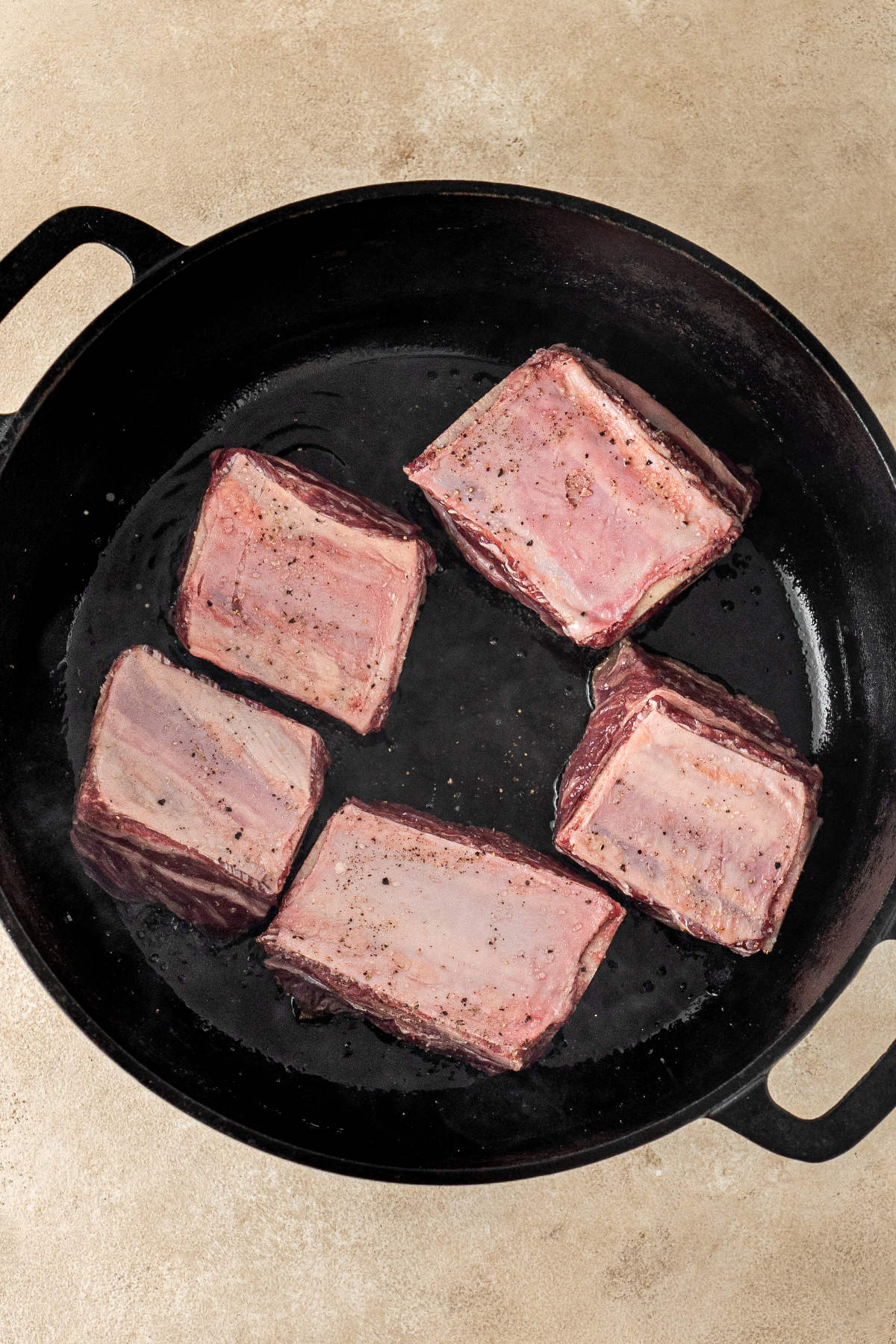 Five raw and seasoned beef ribs ready for cooking in a cast iron pot.