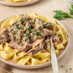 Beef stroganoff served on top of paste with a fork on the plate.